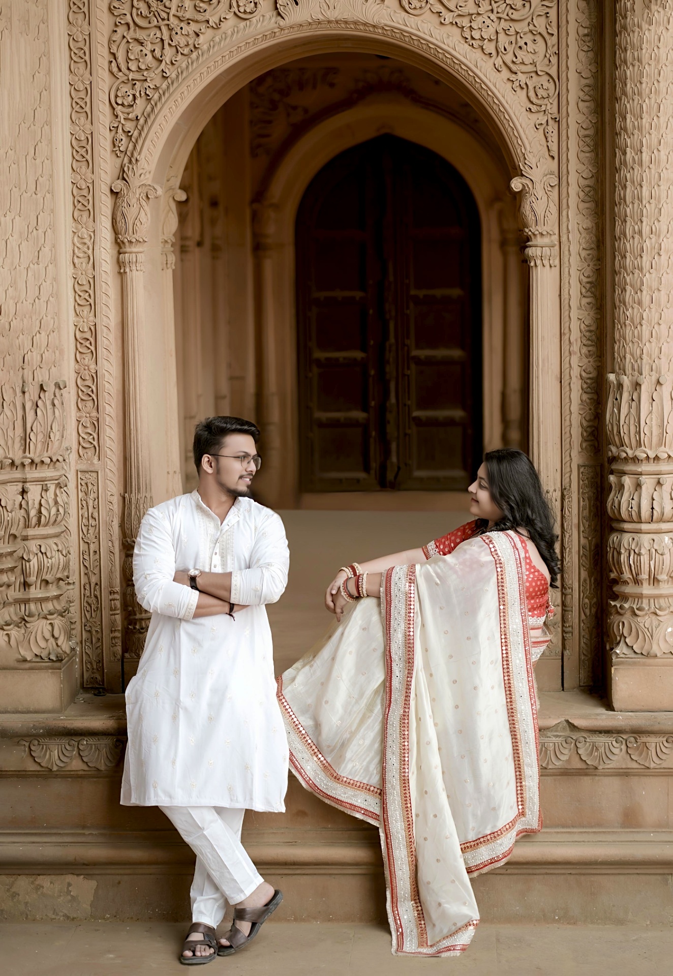 Couple in traditional attire posing under an ornate carved sandstone archway
